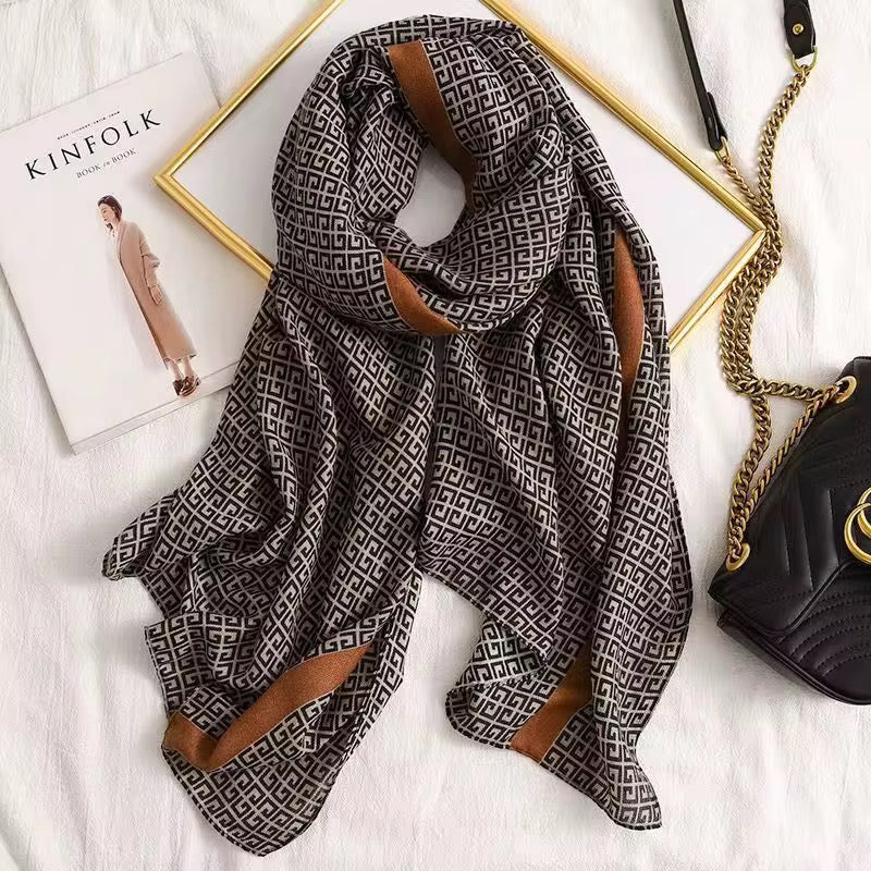 Patterned scarf with brown accents on a white surface with a magazine and handbag.