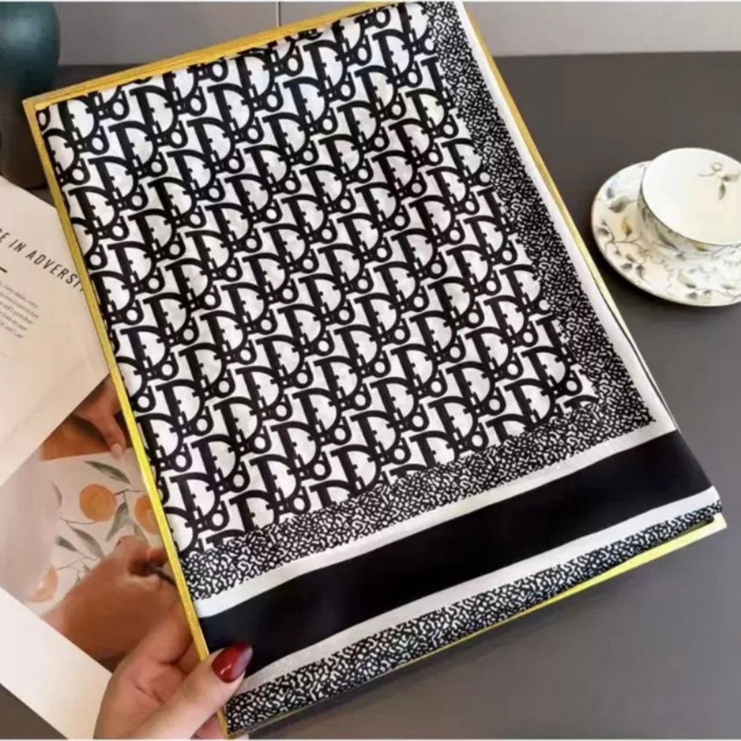 Hand holding designer logo print silk stole showing monogram pattern and striped border detail