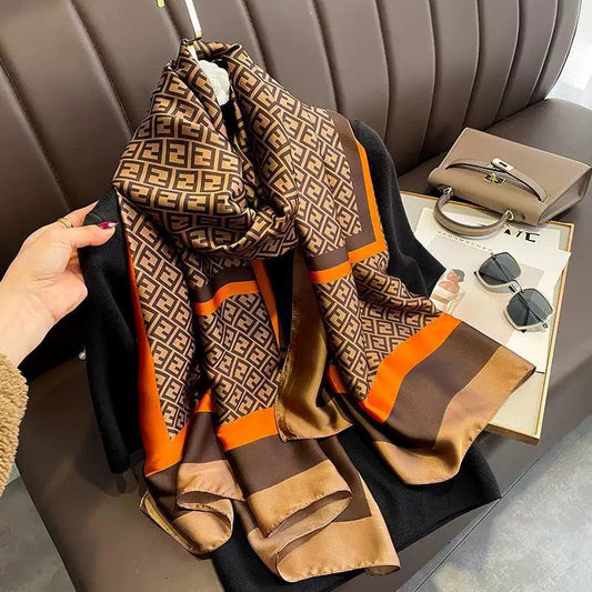 Patterned scarf held by a hand with a magazine and sunglasses on a table in the background.