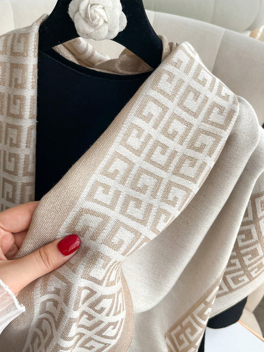 Beige patterned scarf held by a hand with red nail polish