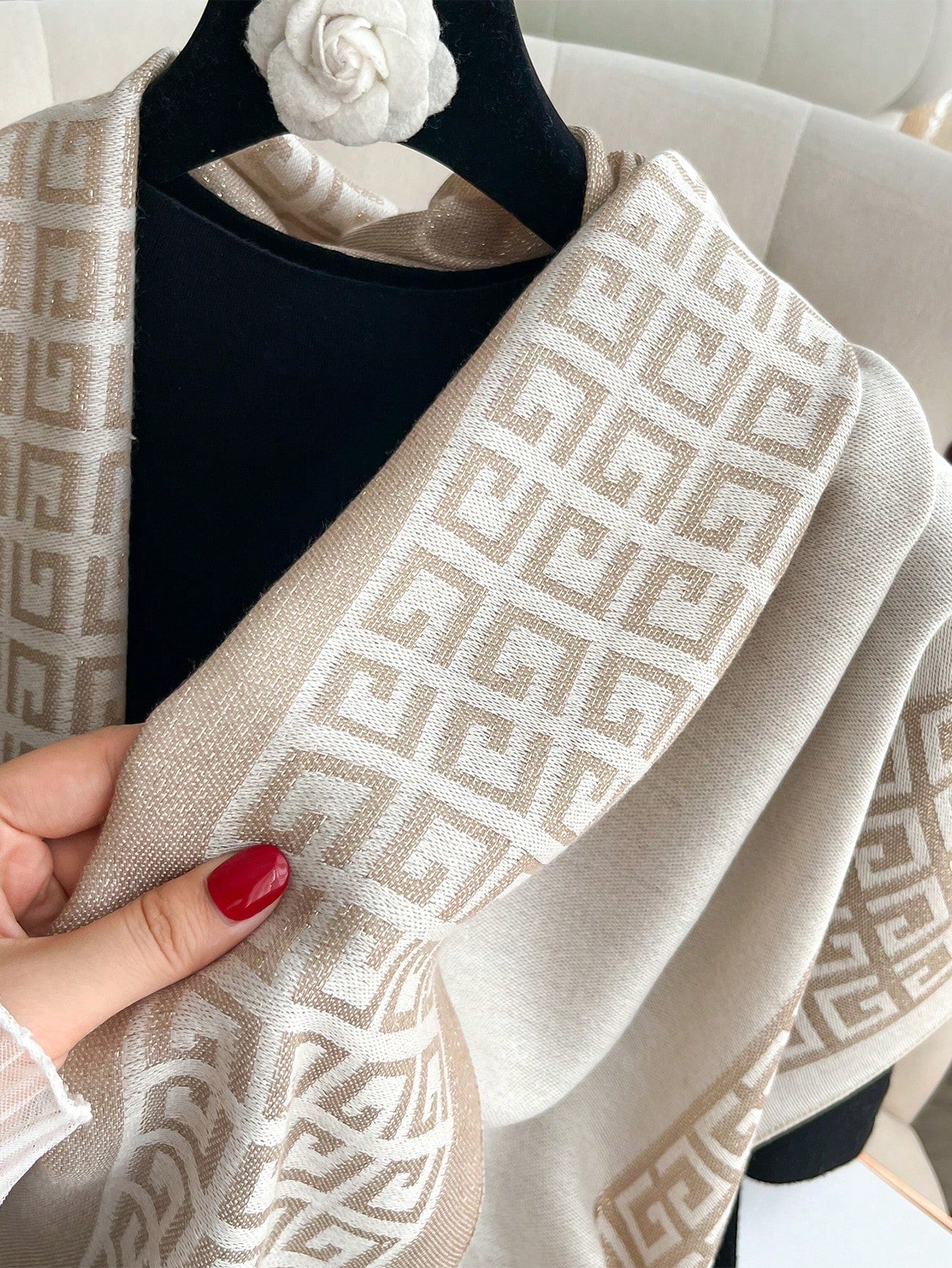 Beige patterned scarf held by a hand with red nail polish