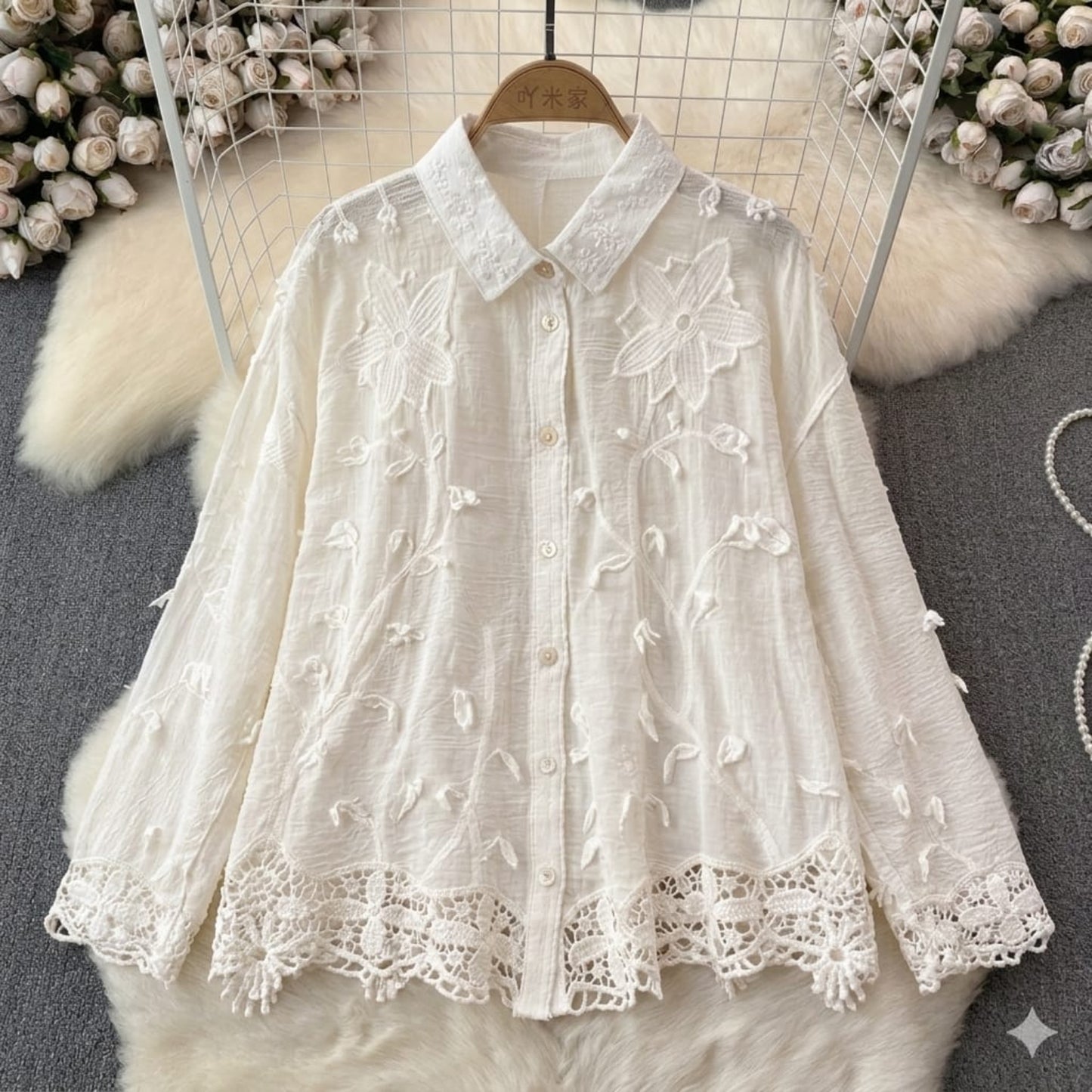 White lace blouse on a hanger with floral patterns against a neutral background