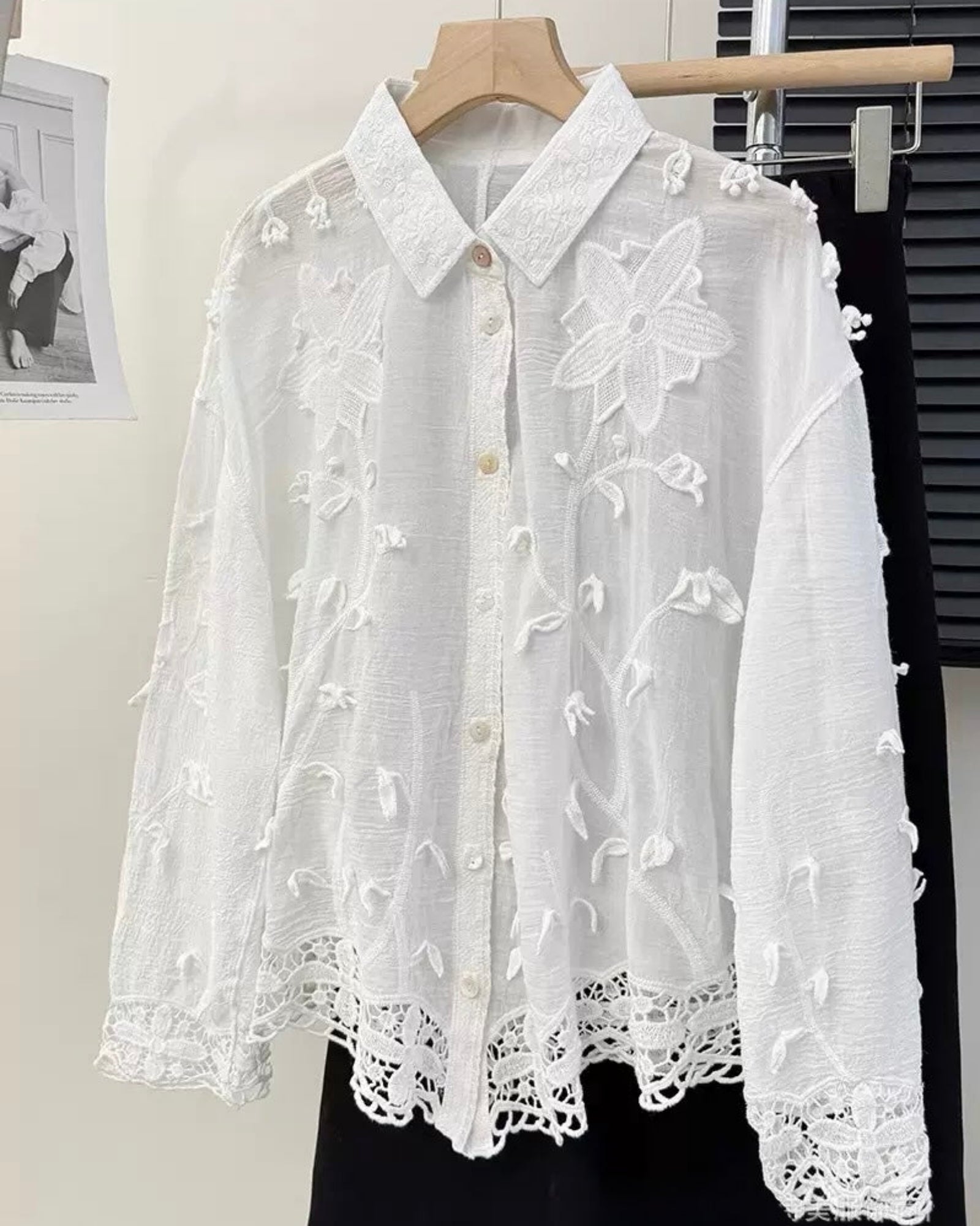 White lace blouse on a hanger against a neutral background