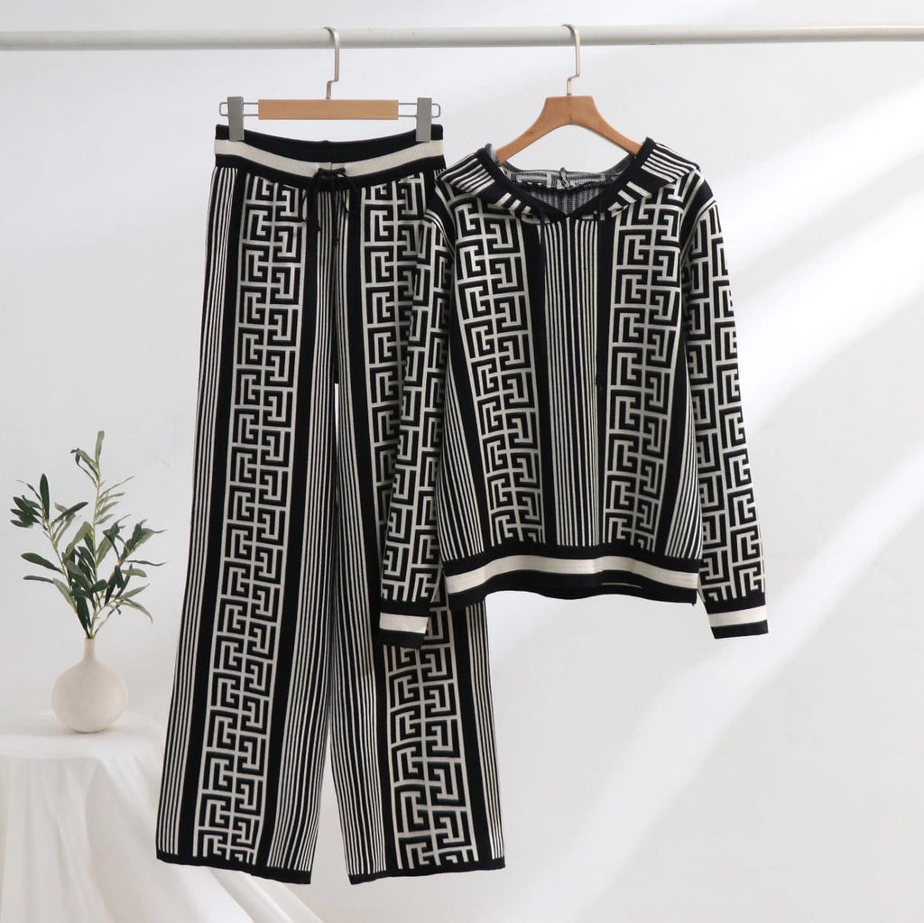 A hooded co ord set displayed on hangers, featuring a geometric pattern with black and white colors. The set includes a long-sleeved top and wide-leg pants.