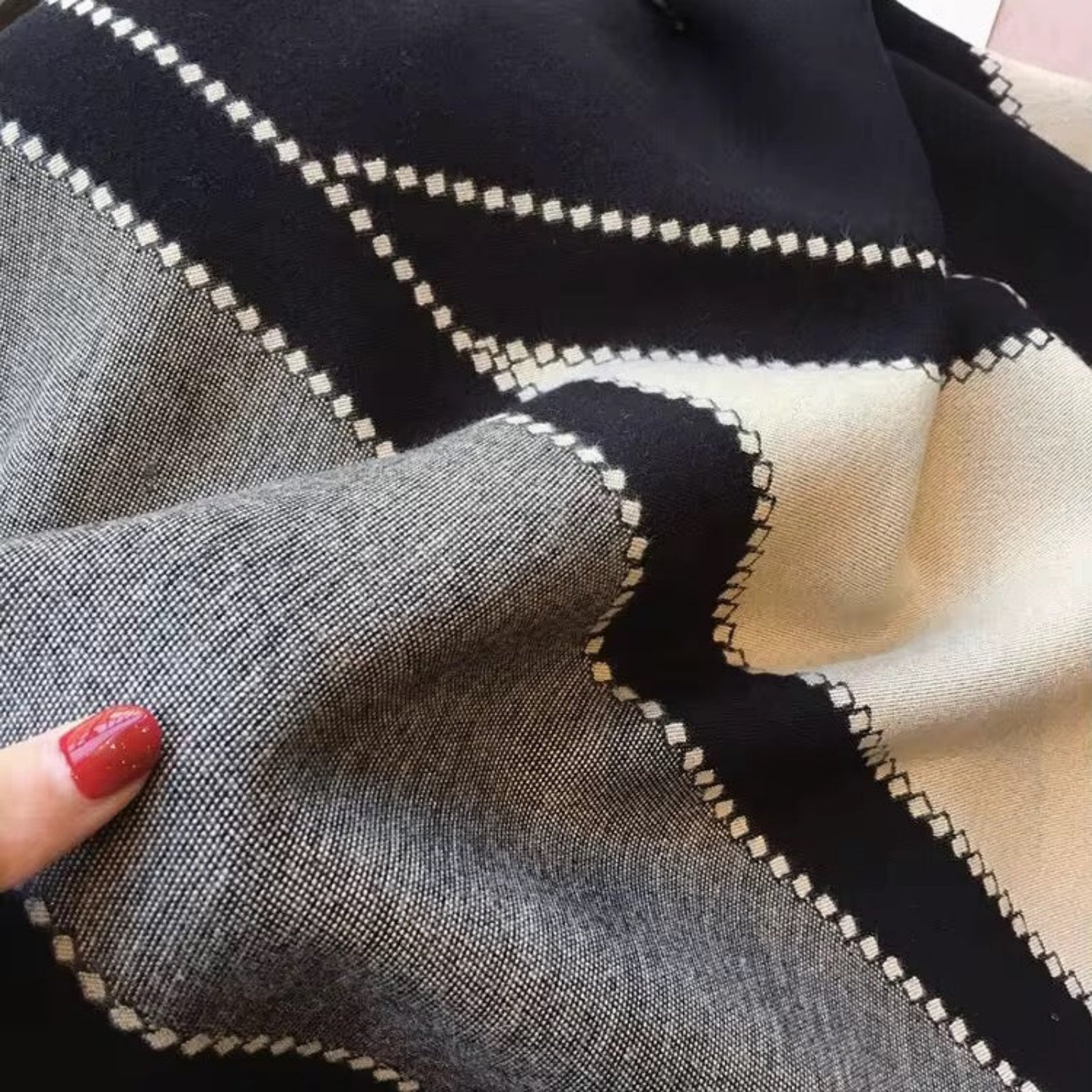 Close-up of fabric with geometric pattern, held by a hand with red nail polish.