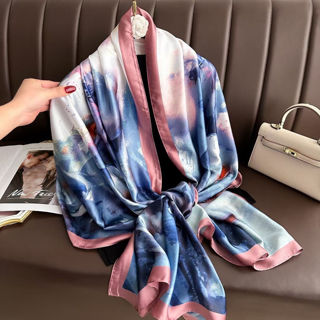 Multicolored scarf draped over a chair with a hand holding it, next to a beige handbag.
