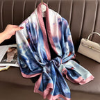 Multicolored scarf draped over a chair with a hand holding it, next to a beige handbag.