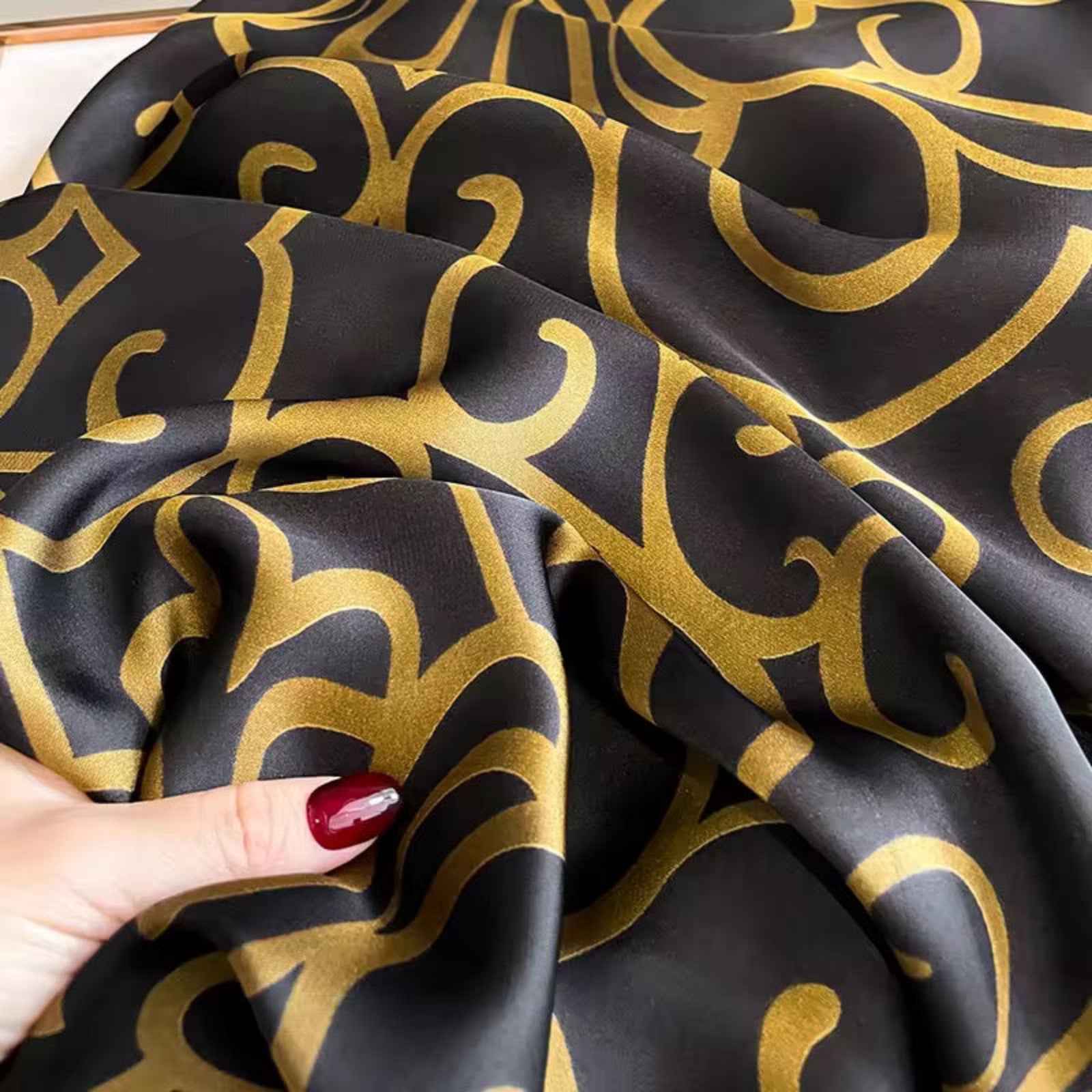 Black fabric with gold patterns held by a hand
