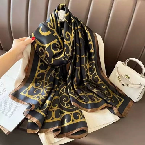 Black and gold patterned scarf held by a hand with a white handbag in the background.