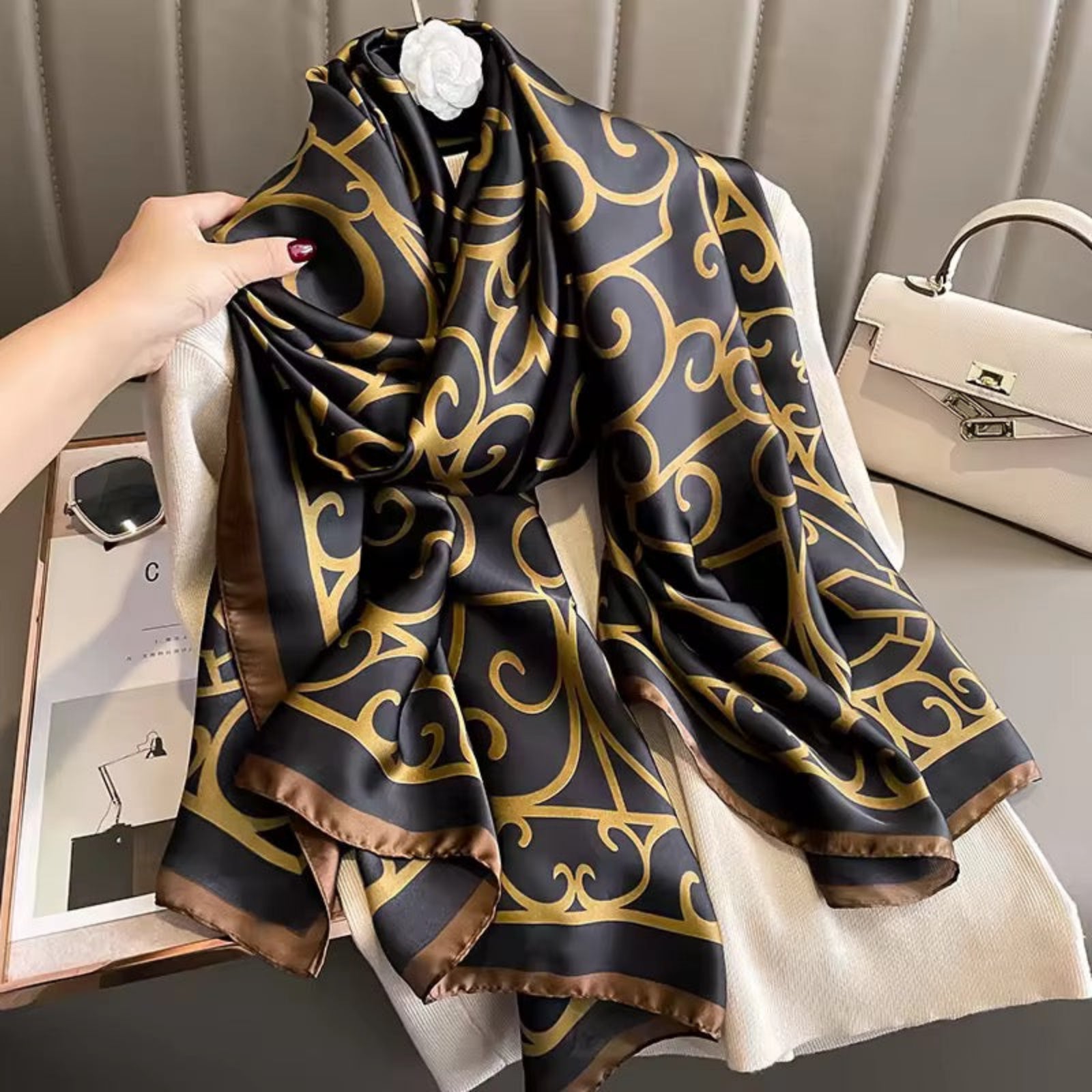 Black and gold patterned scarf held by a hand with a neutral background