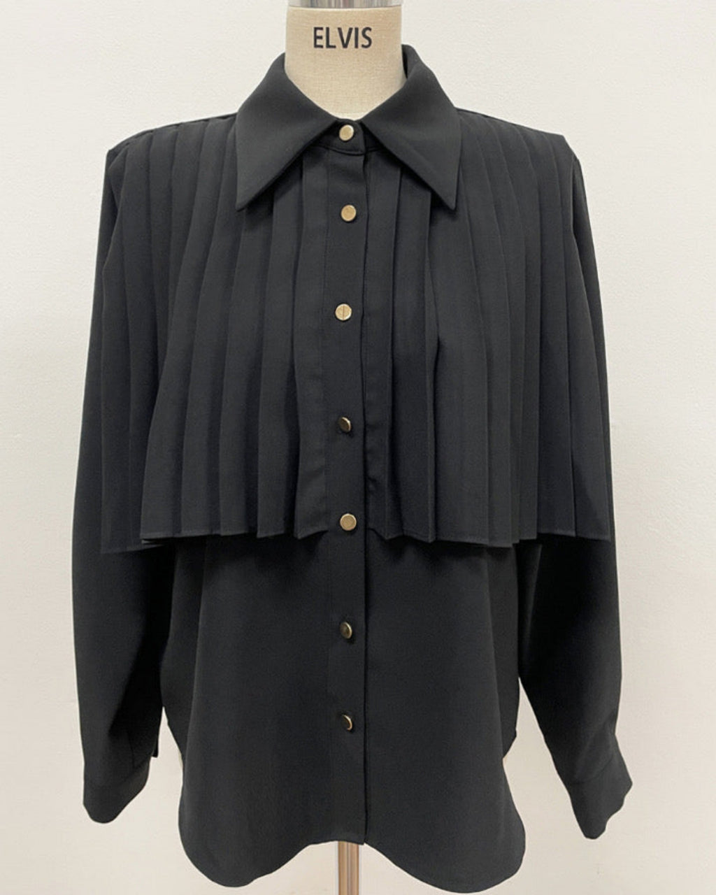 Black pleated cape collar shirt on mannequin - front view showing vertical pleated detail and collar