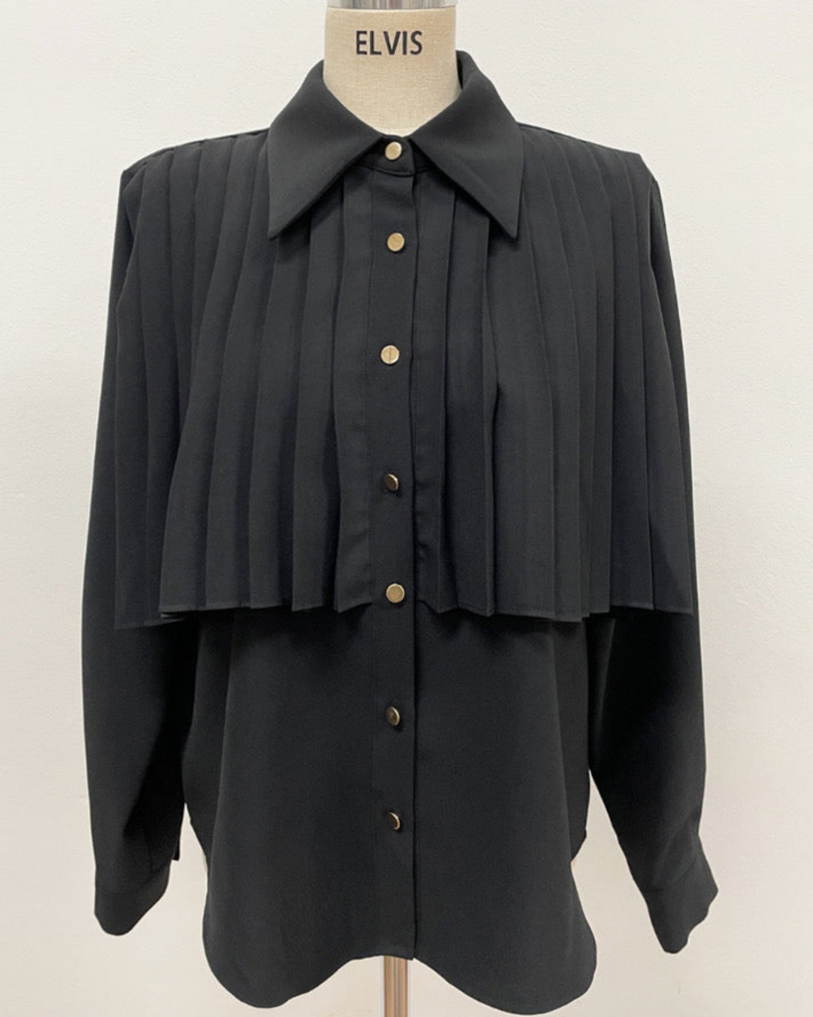 Black pleated cape collar shirt on mannequin - front view showing vertical pleated detail and collar