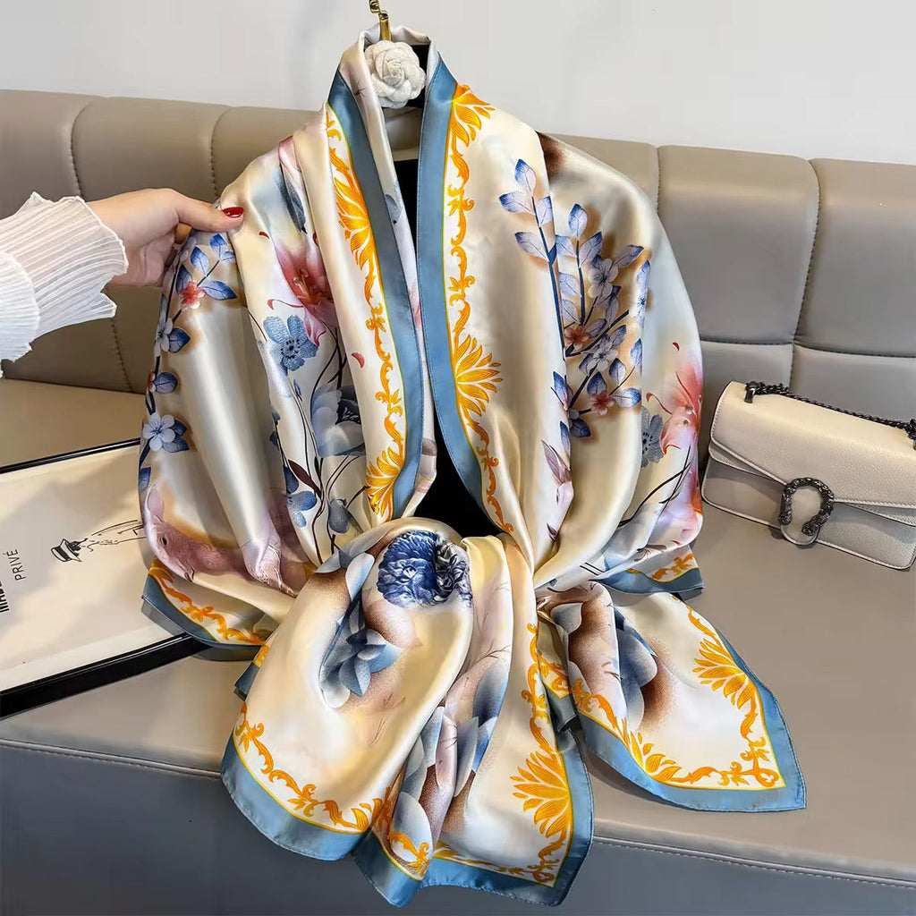 Colorful floral scarf held by a hand on a sofa with a magazine and handbag in the background.