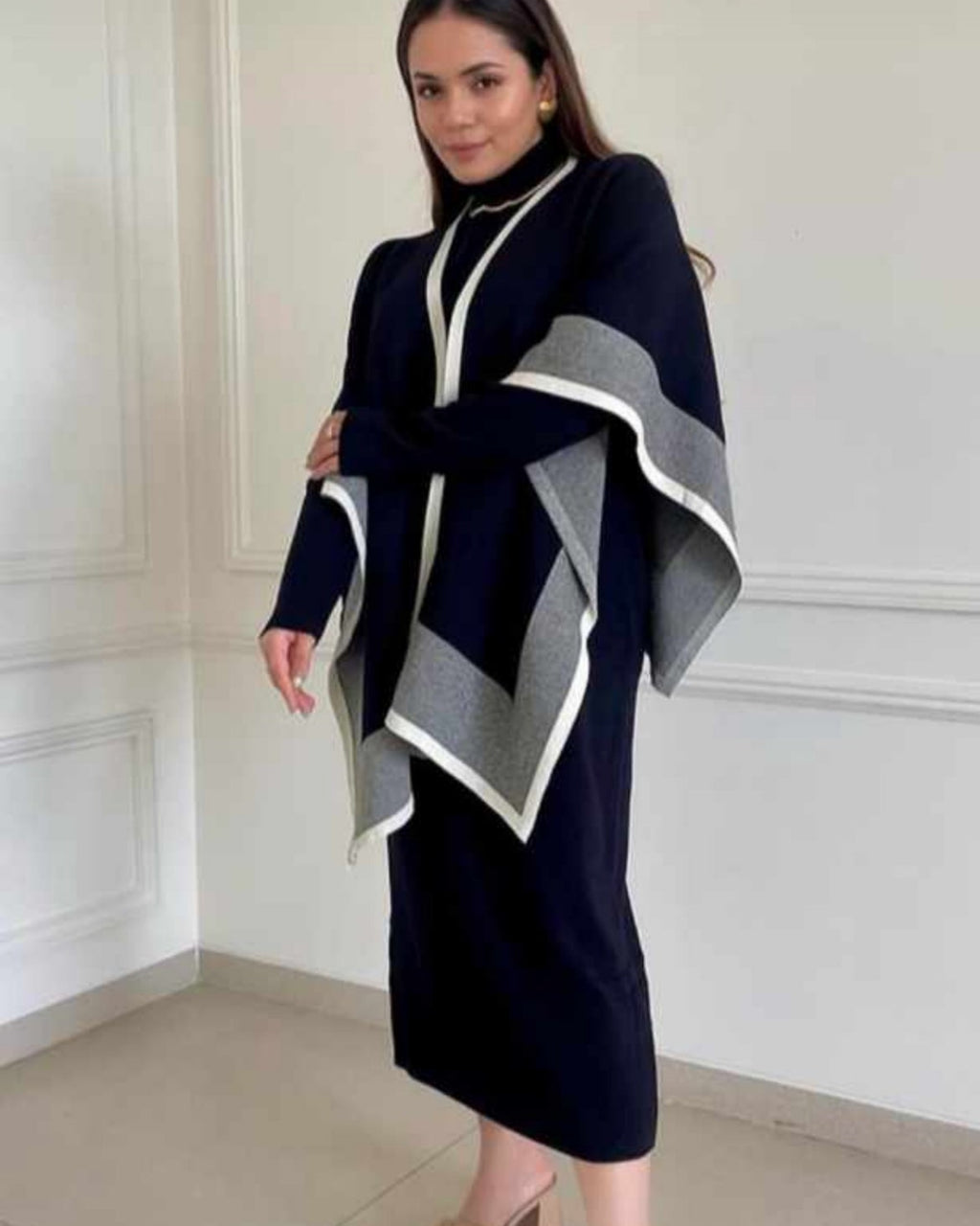 Woman wearing a navy blue dress with a matching poncho in a room with white walls.