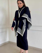 Woman wearing a navy blue dress with a matching poncho in a room with white walls.