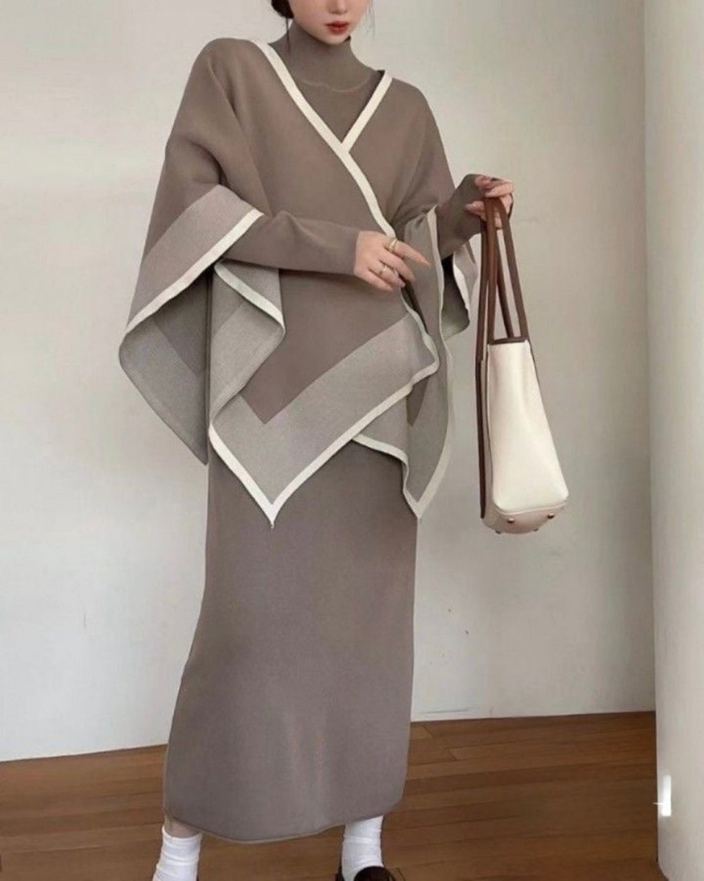 Person wearing a brown dress with a matching shawl, holding a white bag against a plain background.