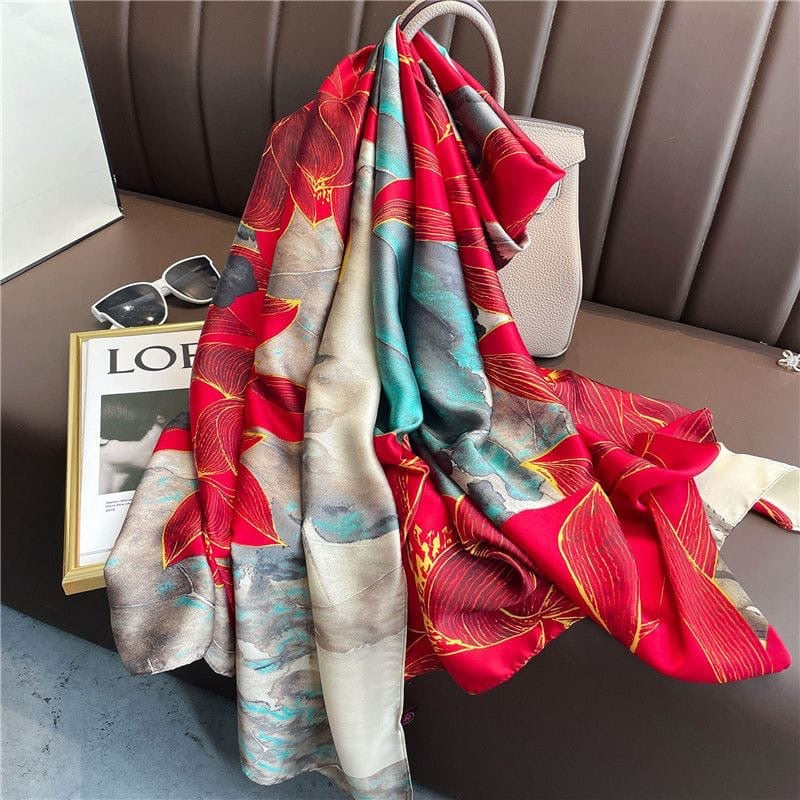 Boxy Luscious Silk Scarf elegantly draped over a handbag, revealing its flowing silk texture, statement floral artwork and sophisticated blend of crimson, teal and neutral tones.