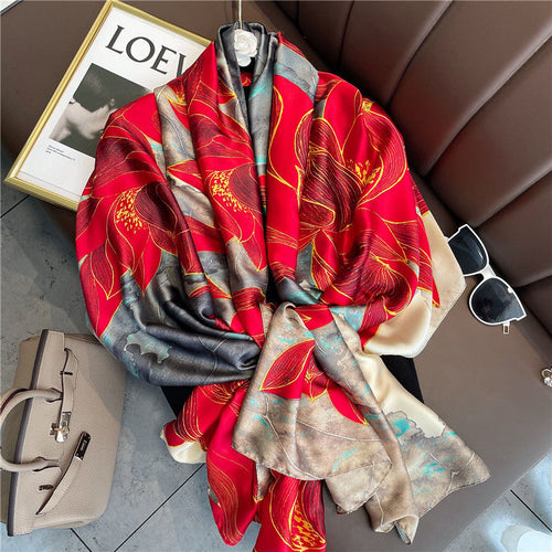 Boxy Luscious Silk Scarf displayed in a luxurious flat lay arrangement, showcasing vibrant red floral blooms with intricate gold accents on a teal, grey and ivory marbled base.