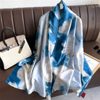 Blue and white patterned scarf draped over a brown sofa with a handbag and sunglasses on a table.