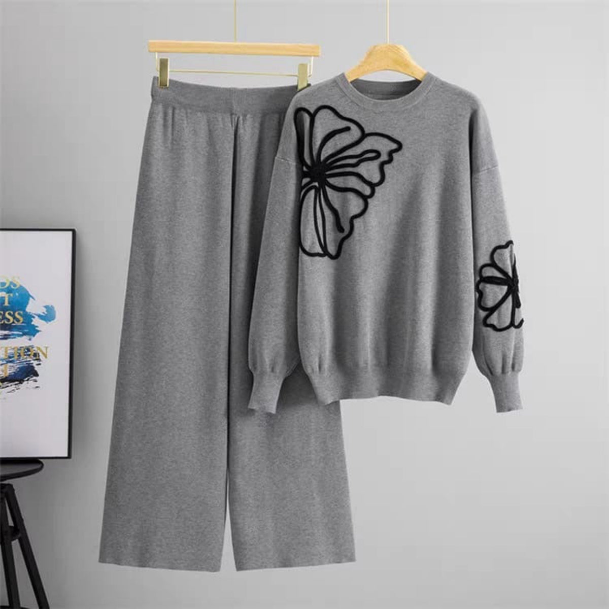 Gray sweater with butterfly design and matching pants on hangers against a gray background.