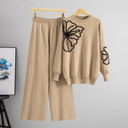 Beige sweater and pants set with butterfly design on a hanger against a gray background.