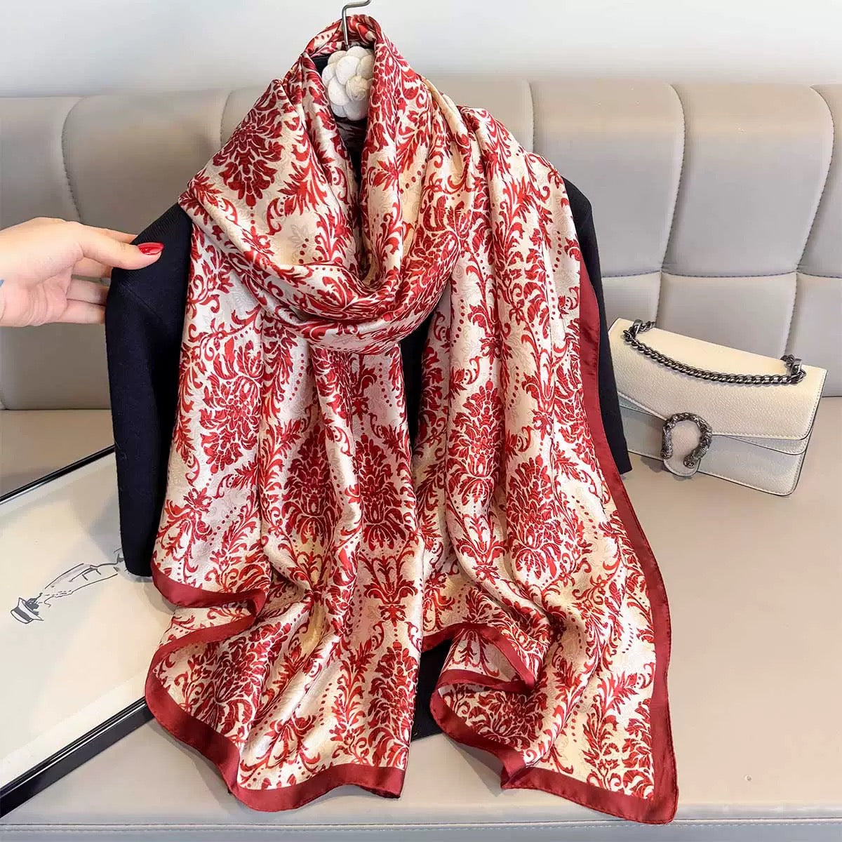 Red and white patterned scarf draped over a black jacket on a light gray couch.