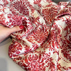 Red and white patterned fabric being held by a hand with red nail polish.