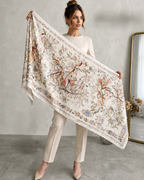 Woman holding a large floral and nature-themed scarf in a minimalistic room.