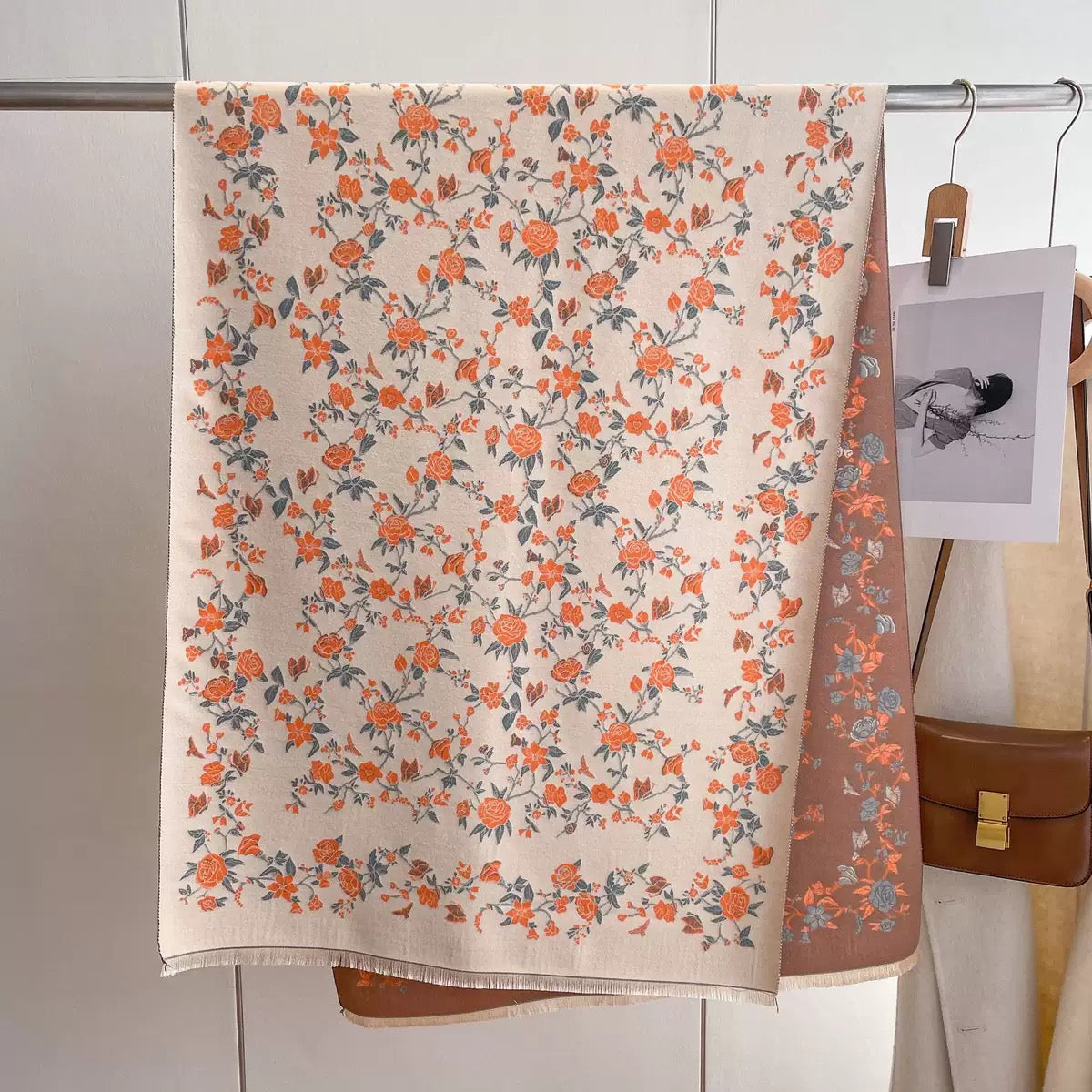 Floral patterned towel hanging on a rack with a brown bag and photo in the background.