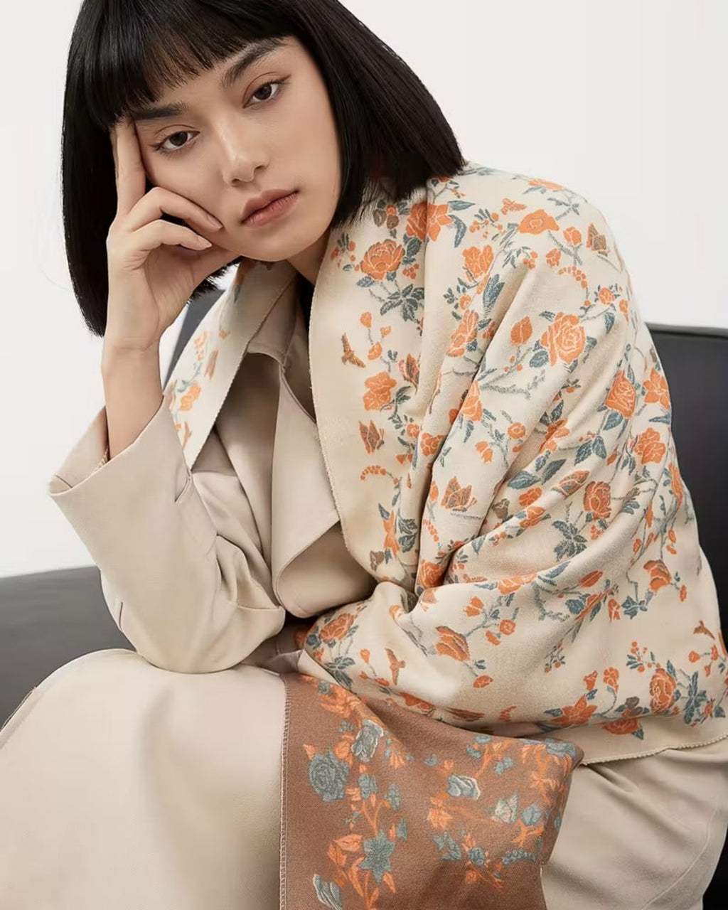 Woman wearing a floral scarf and beige coat against a white background