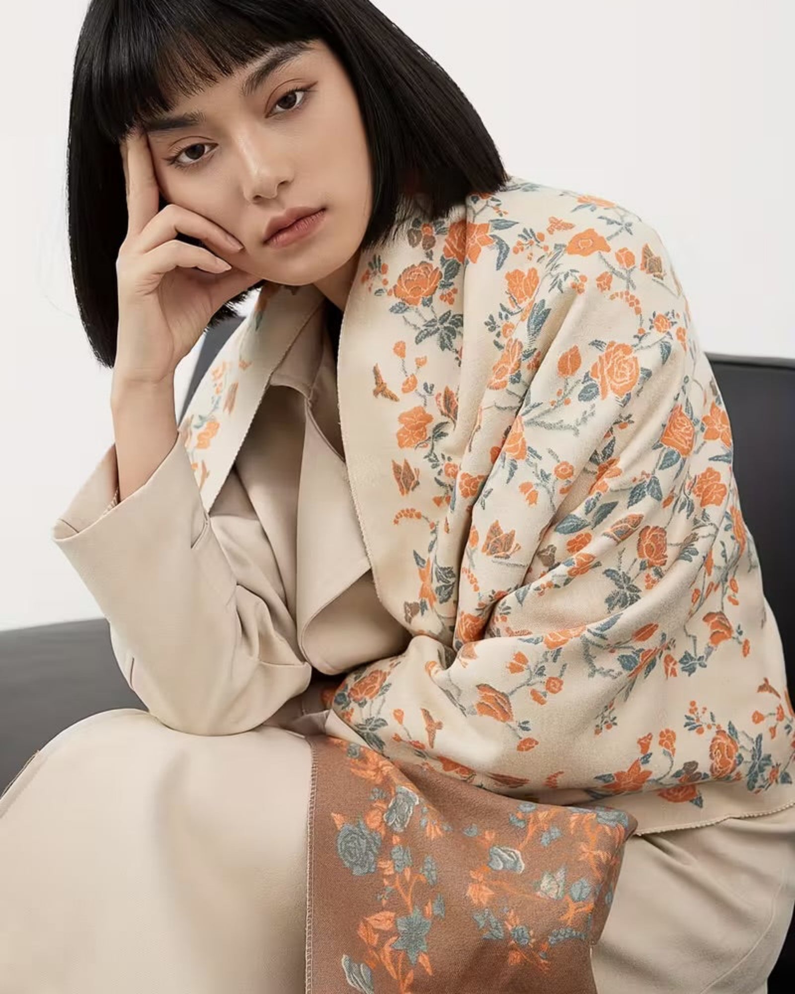 Woman wearing a floral scarf and beige coat against a white background
