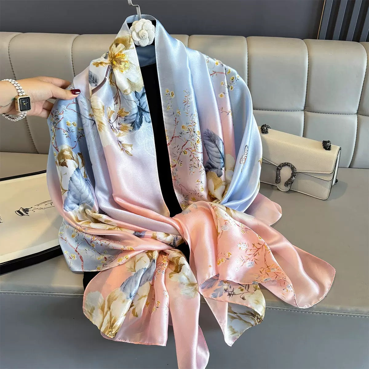 Floral and bird patterned scarf draped over a surface with a hand holding it.