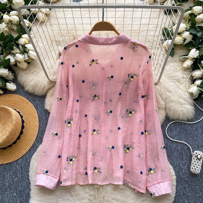 Pink embroidered blouse on a hanger with decorative elements in the background