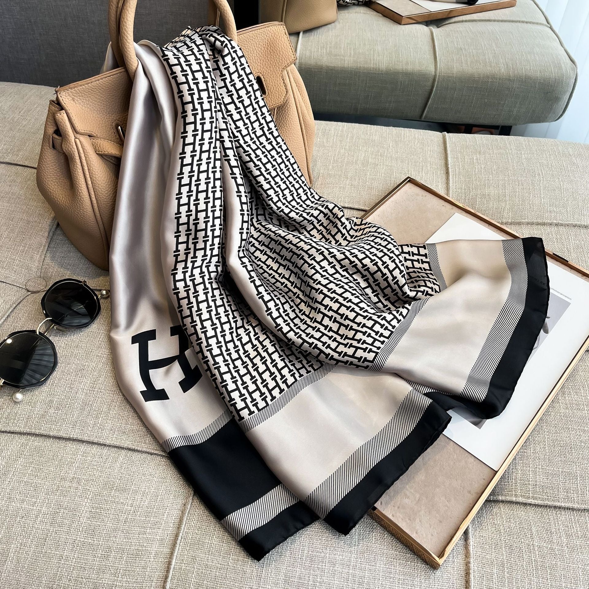 Black and white patterned scarf draped over a beige handbag on a couch.