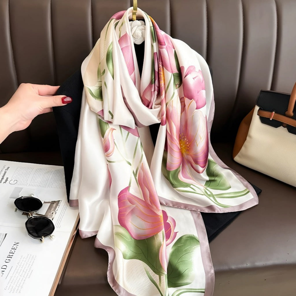 A silk stole with a floral pattern in pink, green, and white, draped over a chair with a hand holding one end of the stole.