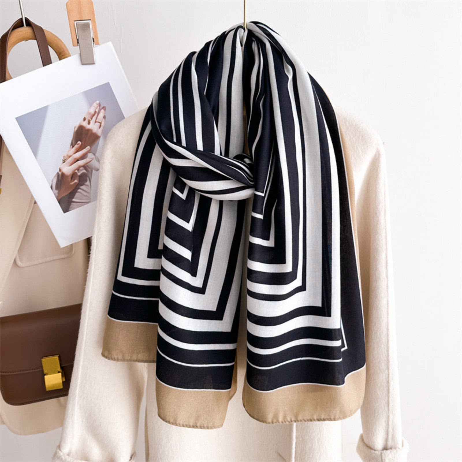 Black and white striped scarf draped over a beige jacket with a handbag and photo in the background.