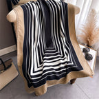 Black and white striped scarf draped over a beige chair with a handbag and sunglasses on a table in the background.