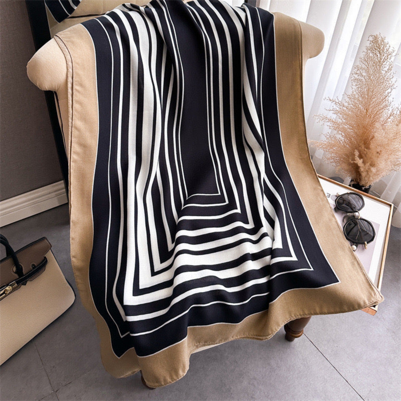 Black and white striped scarf draped over a beige chair with a handbag and sunglasses on a table in the background.
