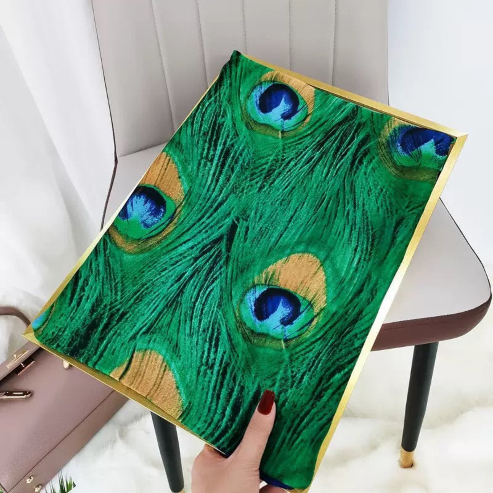 Hand holding a decorative item with peacock feather design on a chair.