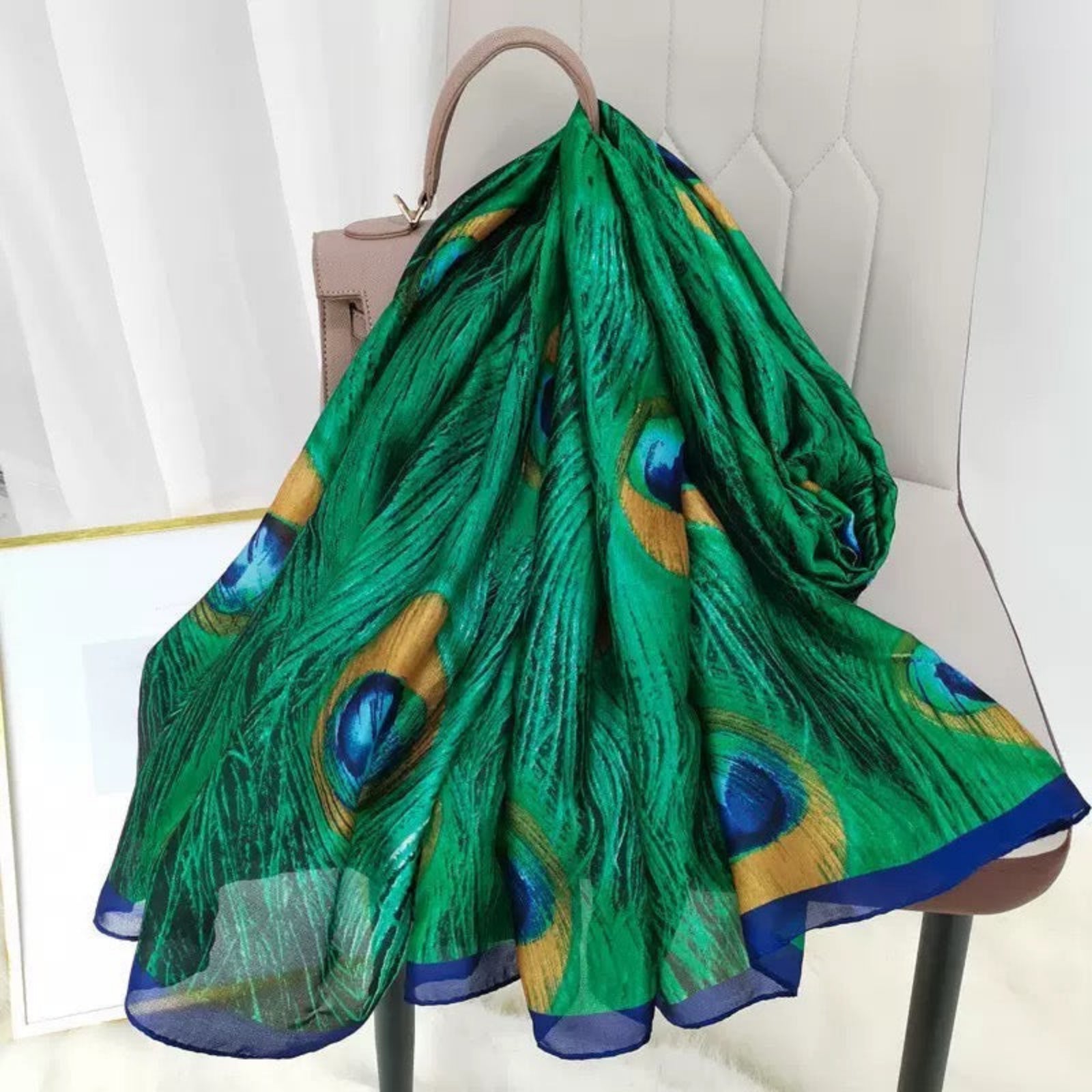 Green peacock feather patterned scarf draped over a chair with a neutral background