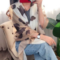 Person wearing a beige scarf with brown dog prints, sitting on a chair.