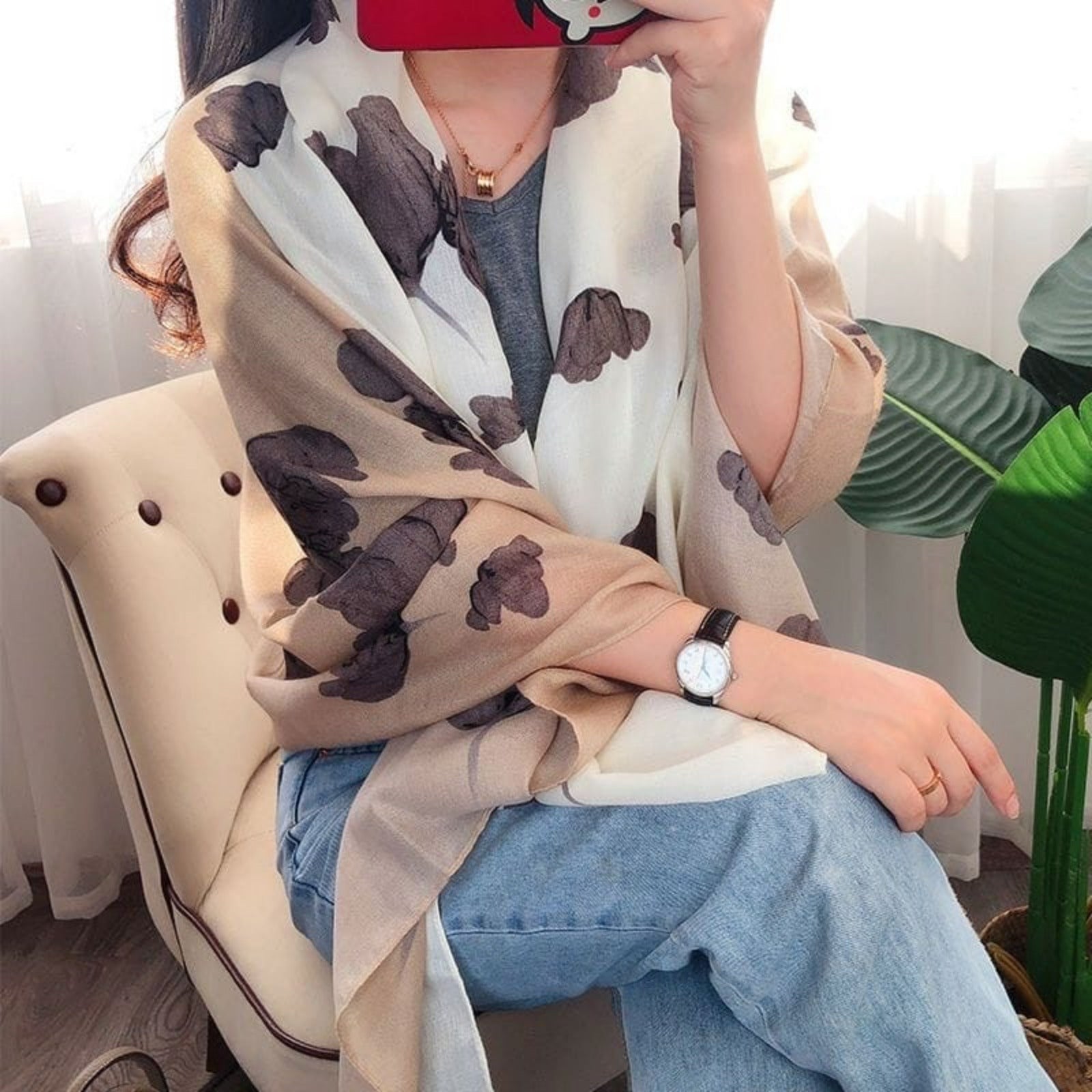 Person wearing a beige scarf with brown dog prints, sitting on a chair.