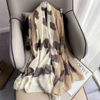 Beige scarf with brown butterfly patterns draped over a chair, with LOEWE branding visible.