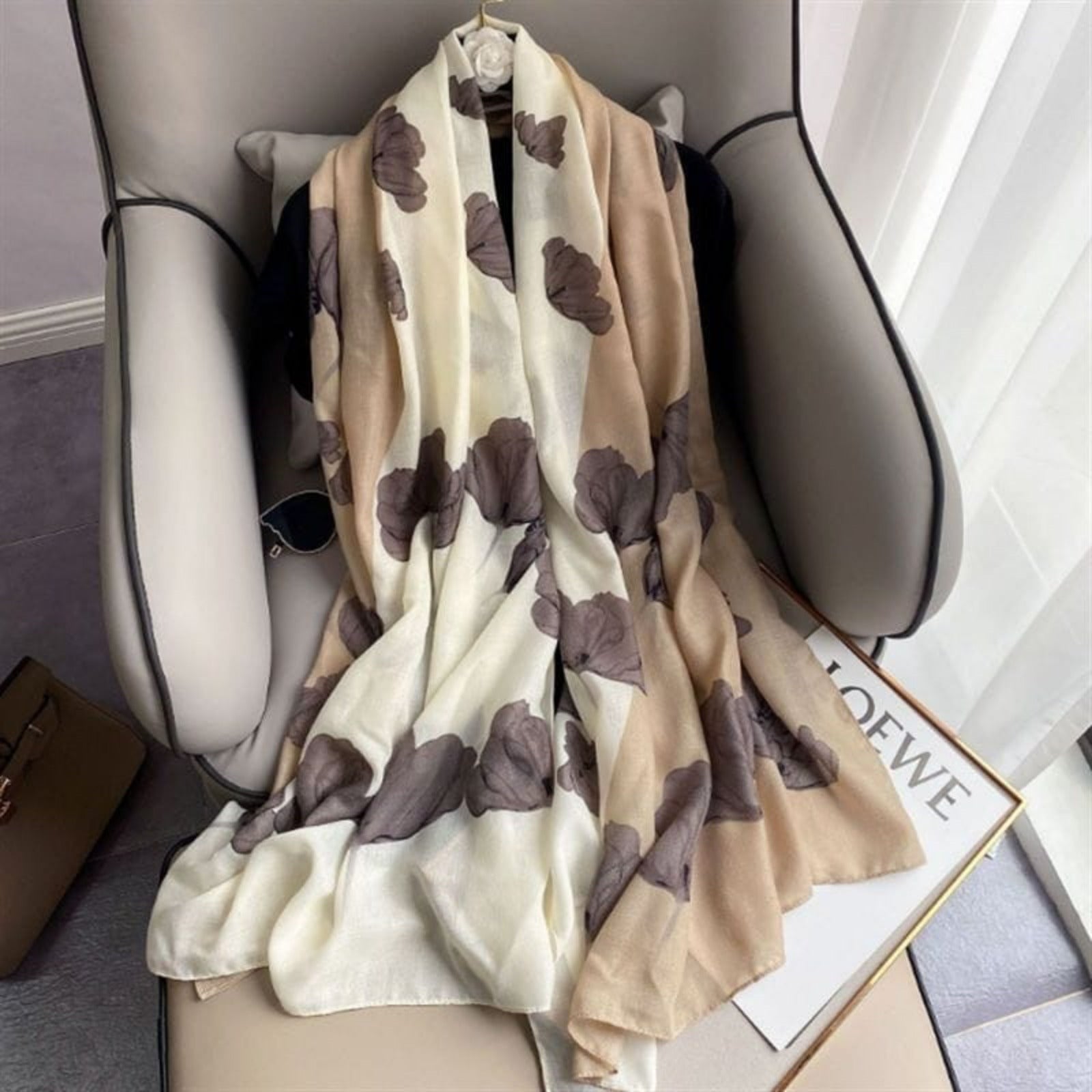 Beige scarf with brown butterfly patterns draped over a chair, with LOEWE branding visible.