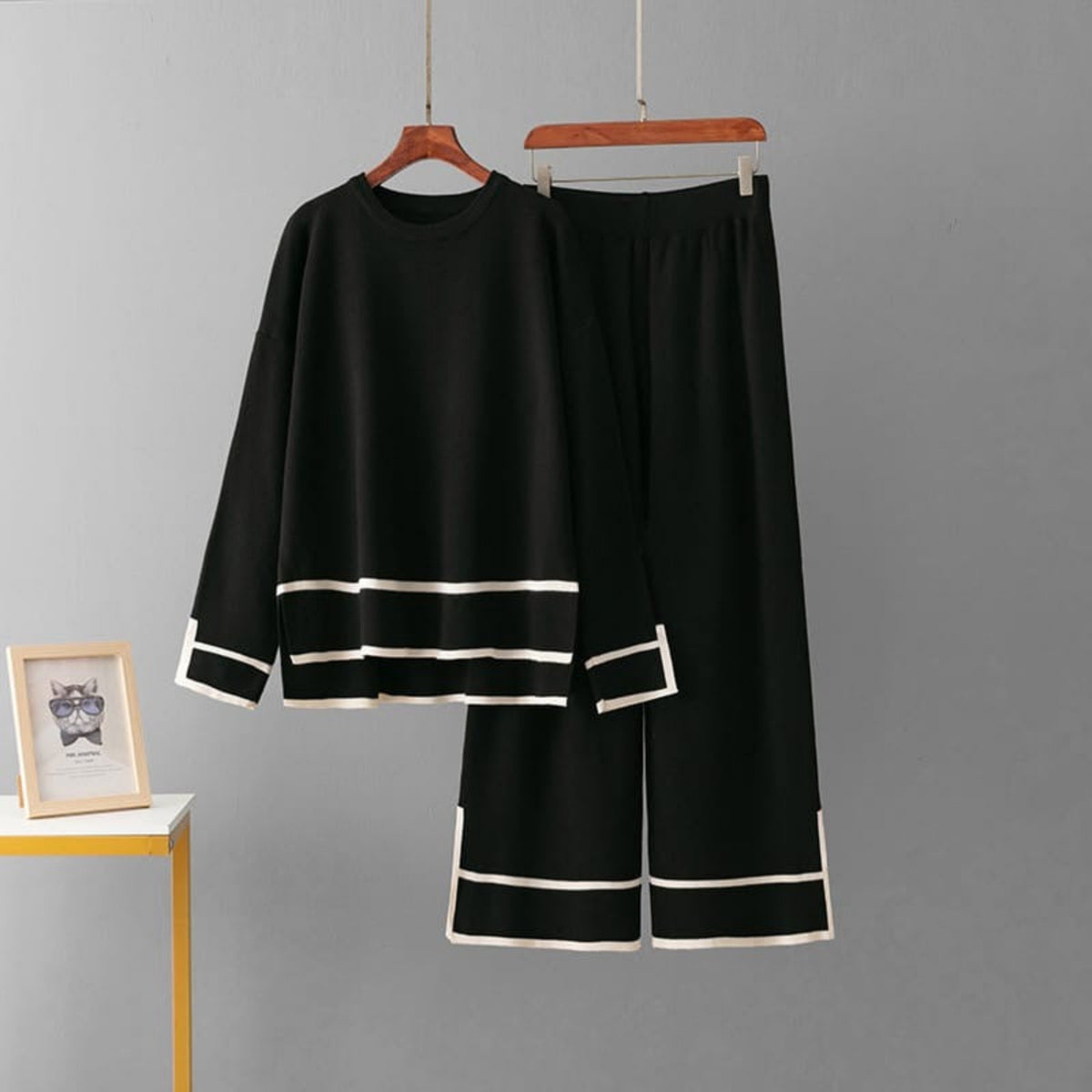 Black outfit with white trim on hangers against a gray background