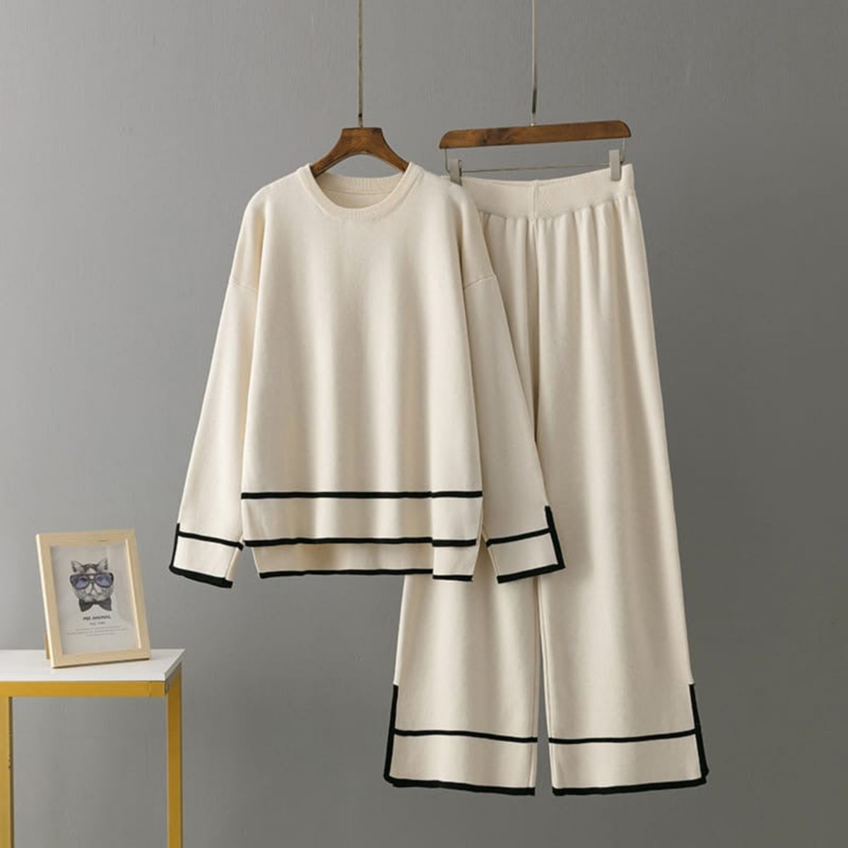 White outfit with black trim on hangers against a gray background