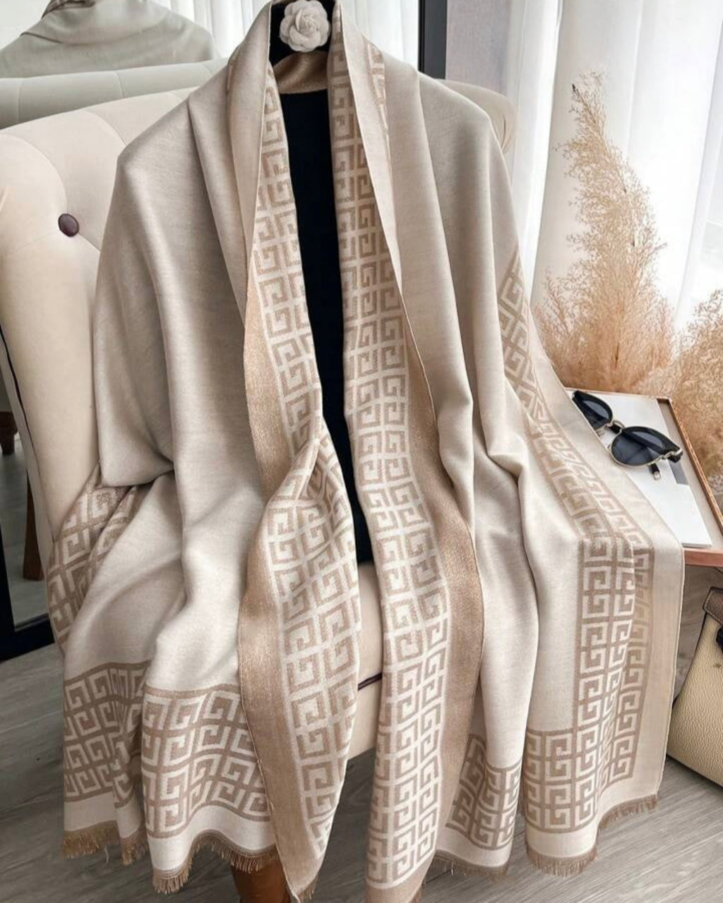 Beige patterned scarf draped over a chair with a neutral background