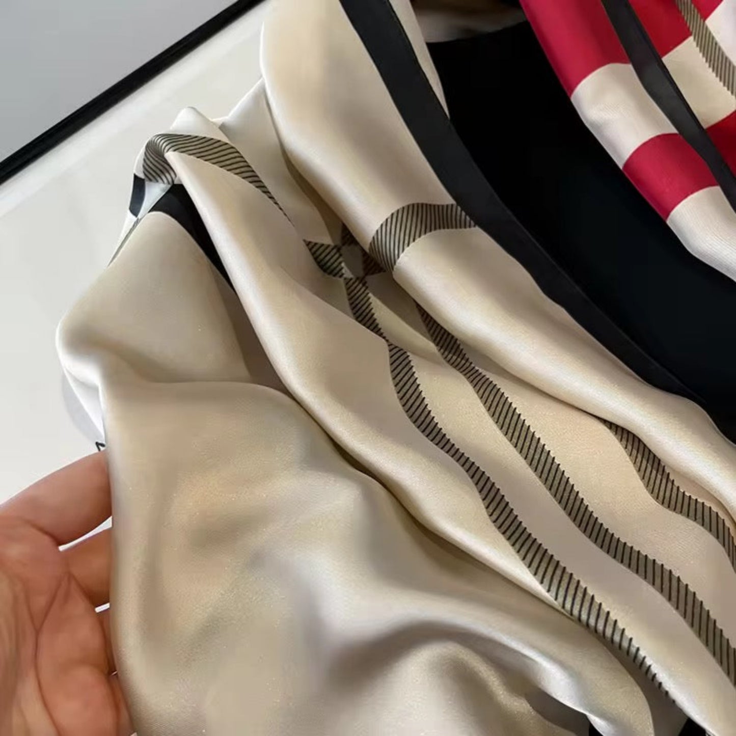 Close-up of a beige scarf with black stripes held by a hand, with a blurred background.