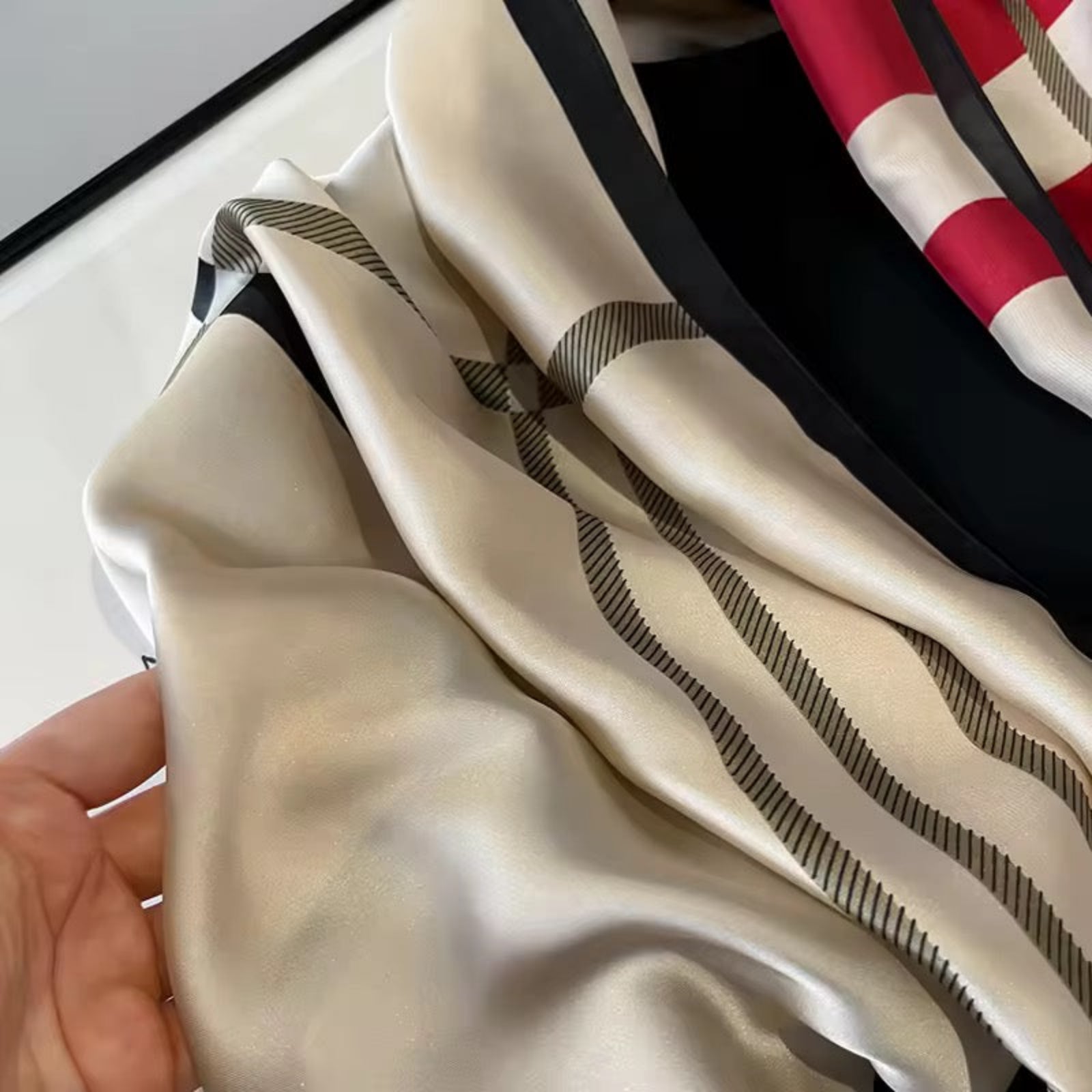 Close-up of a beige scarf with black stripes held by a hand, with a blurred background.