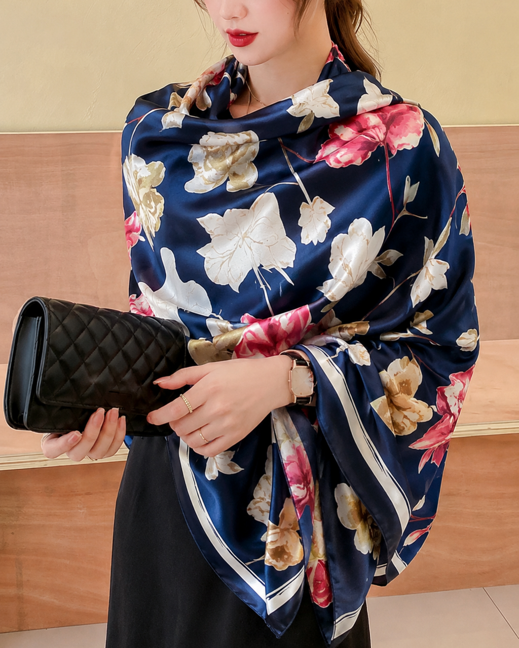 Woman wearing a floral scarf holding a black clutch against a wooden background